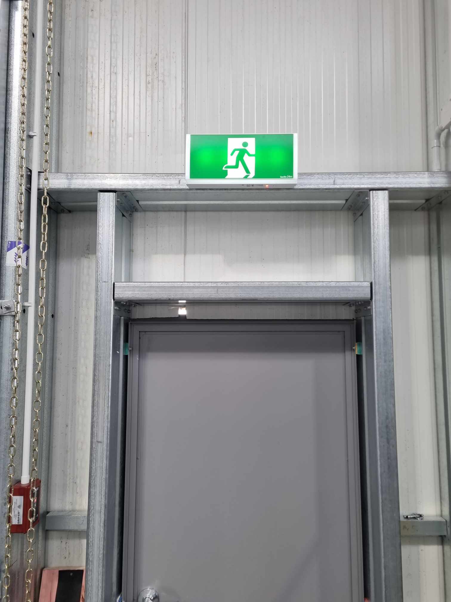 Illuminated emergency exit sign above a warehouse fire door
