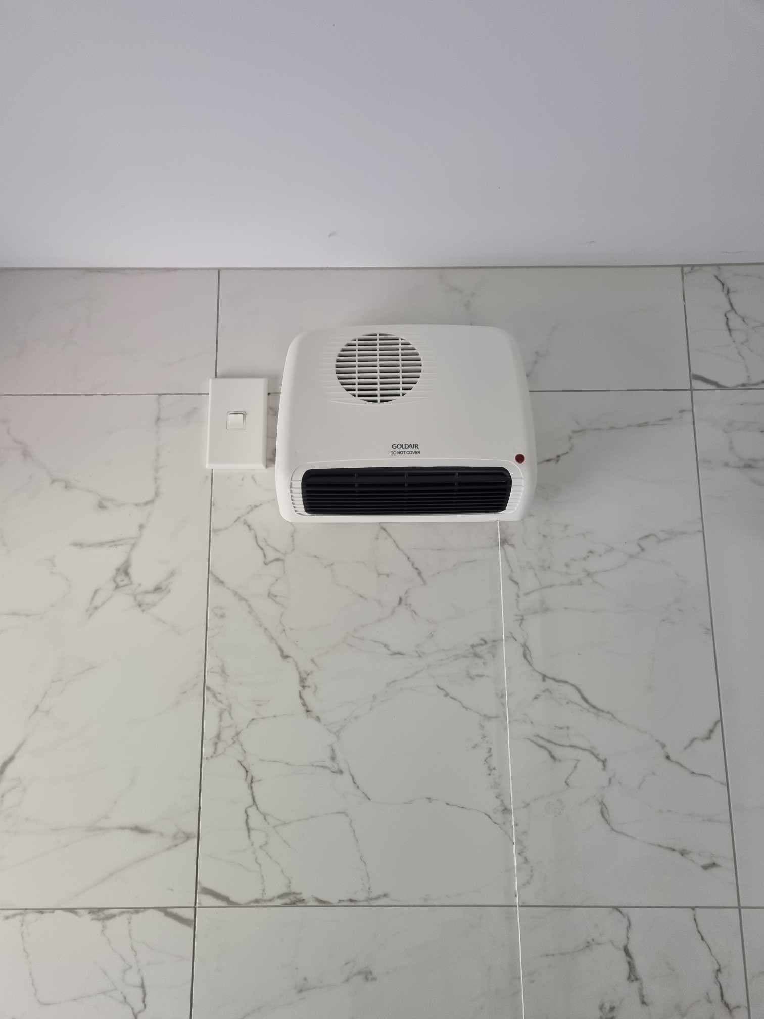 Wall-mounted bathroom fan heater on marble-look tiles